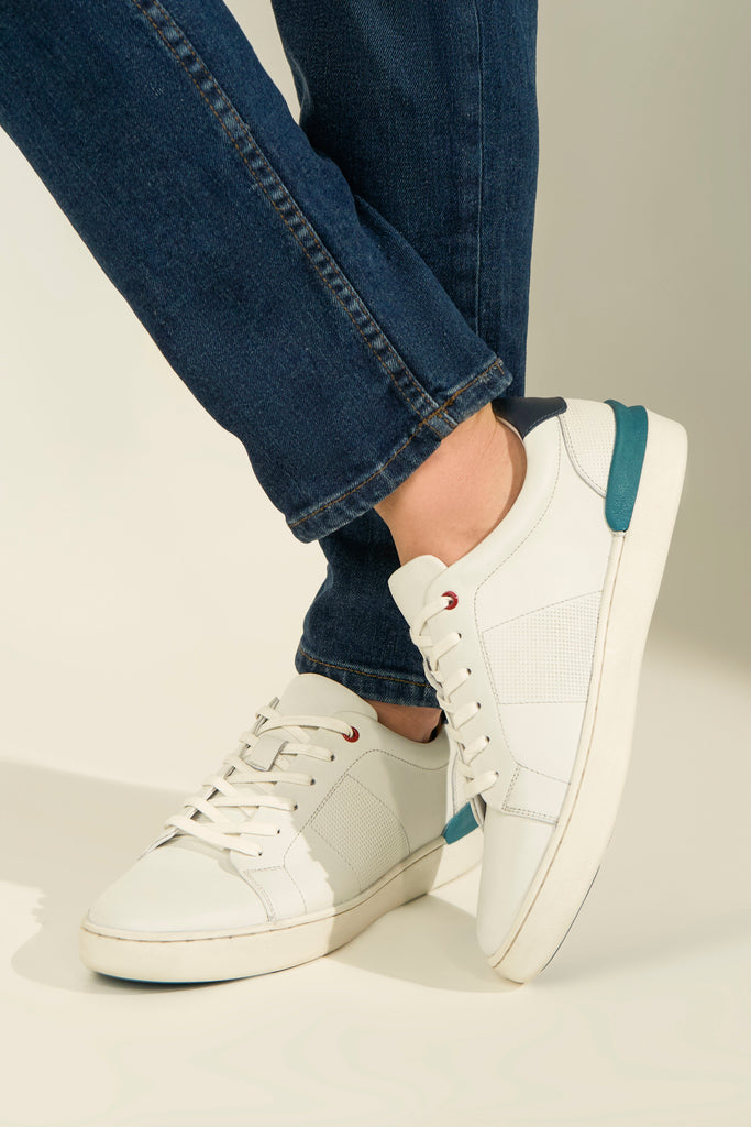 White sneakers with blue accents worn with blue jeans on a neutral background