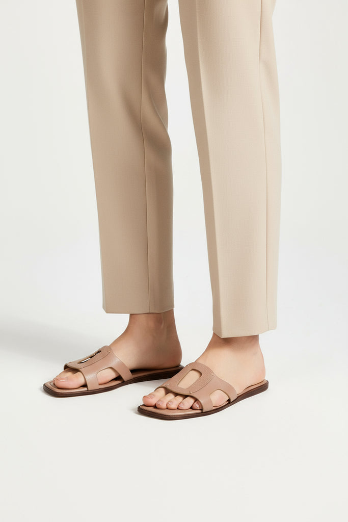 Person wearing beige sandals and beige pants on a white background